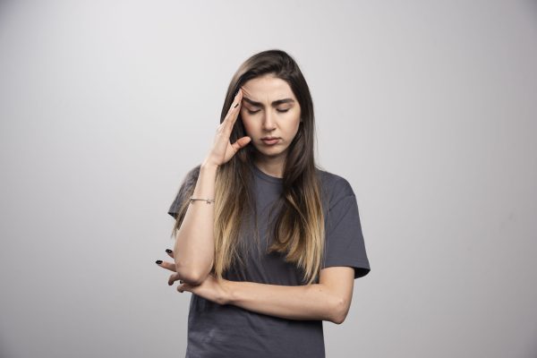 Portrait of young woman touching her head posing over gray background. High quality photo